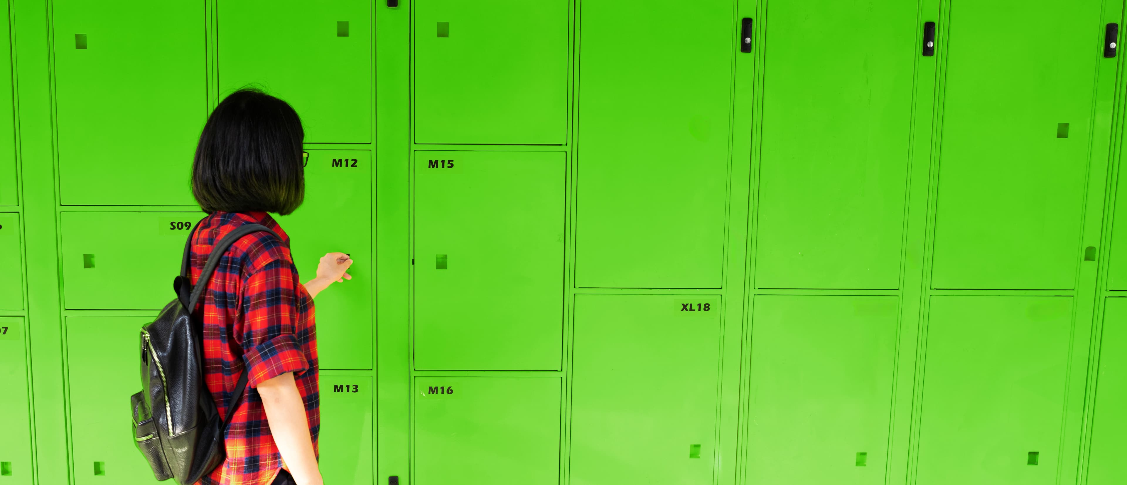 A person storing luggage in a green locker facility in Australia.